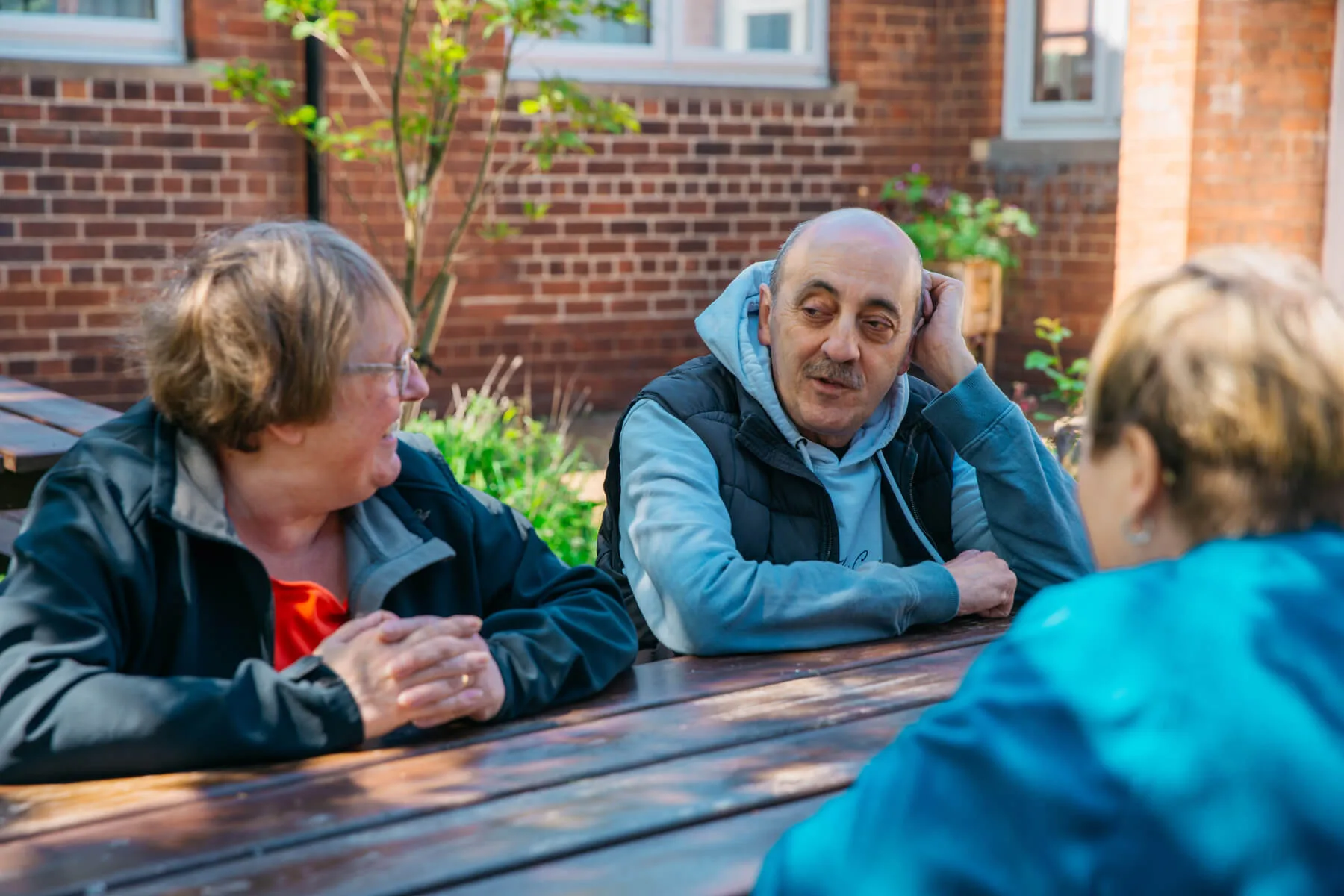 Man and Two Women Speaking At Outside Picnic Table