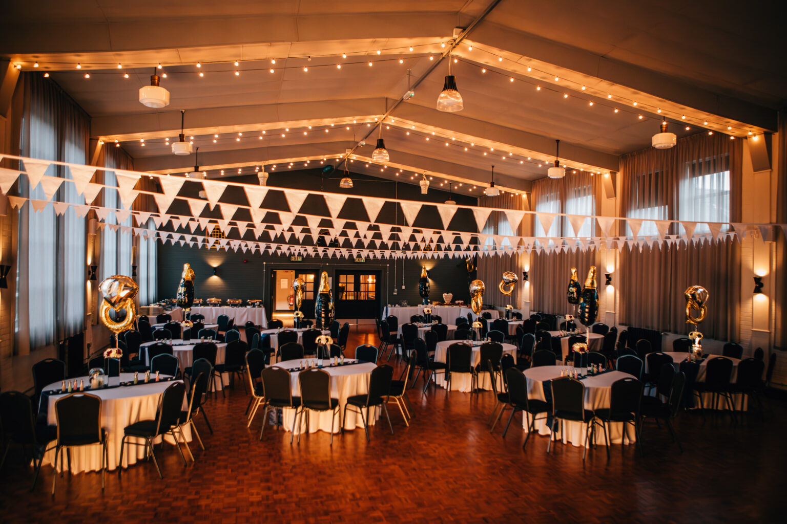 A room lit up with orange coloured lighting, round tables and white flags